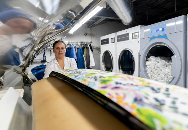 Latin american female worker at a laundry service ironing textiles in an industrial steamer - Business concepts